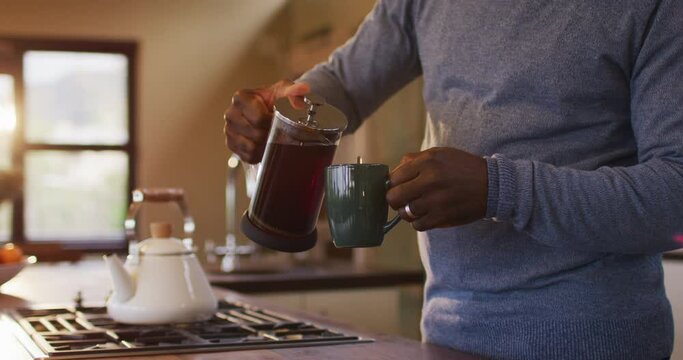 Midsection of african american senior man in kitchen pouring coffee from pot