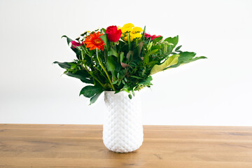 Home interior decor, bouquet colorfol in a white vase and white wall on a wooden table background modern decoration for home, copy space