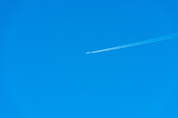 the trace of the plane in the sky. White traces of a jet stream from the combustion of aviation fuel. A passing plane draws white lines on a blue sky without clouds.