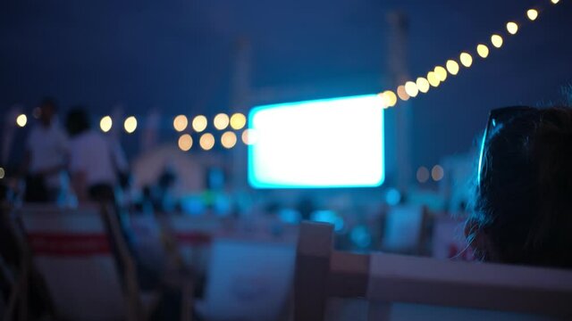 Caucasian Woman Watching Movie in Open Air Beach Cinema during Summer Film Festival