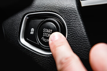 Car start stop system with finger pressing the button. Car driver starting the engine keyless.