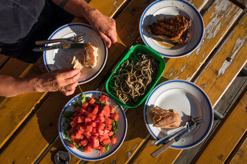 Dinner plates on a wooden table outdoors with salad, pasta and grilled pork chops.