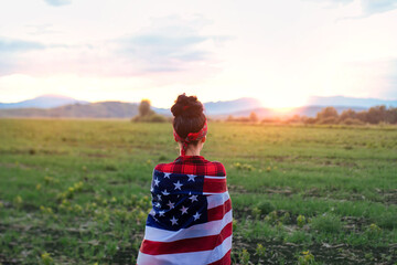A young happy girl runs carelessly and jumps with open arms across the field at sunset. Holds the US flag. Tinted image. Selective focus.