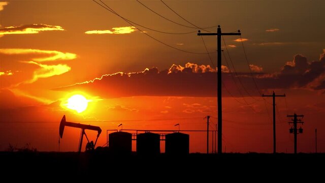 SILHOUETTE: Massive pump jack pumps fossil fuel from the depths of a field in Austin, Texas at sunset. Scenic shot of a pump jack extracting crude oil at a field in Texas on a sunny summer evening.