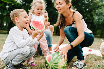 Boy, girls with mother eating watermelon in the summer. Happy family in the park on holidays.