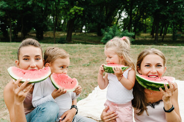 Boy, girls with mother eating watermelon in the summer. Happy family in the park on holidays.