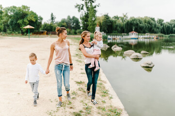Fototapeta premium Two mothers with kids walking on nature on summer day. Mom and son, daughter walk on the beach. Concept of happy family. Close Up.