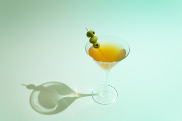 Martini glass filled with orange drink and olives on stick against turquoise sunny background. Minimal summer refreshment concept.