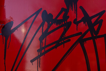 metal surface of the wall painted in red is covered with smeared traces of black paint, vandalism in the urban environment. - Powered by Adobe