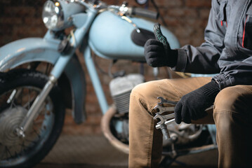 A motorcycle mechanic is showing a thumbs up gesture on the old motorbike background.