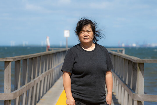 An Asian middle aged woman on a jetty with a blue ocean and sky in the background. Picture from Scania county, Sweden