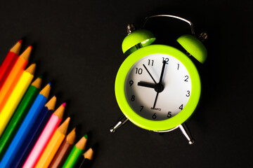 Close-Up Of light green Alarm Clock With Colored Pencils black Background. time to draw. Art school. Selective focus