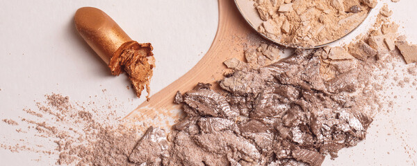Crushed beige face finishing and liquid powder, smashed lipstick and cracked eyeshadow. Macro texture of make-up on beige background