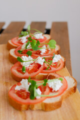 white bread bruschetta with tomato, cheese and micro-greenery on a wooden board