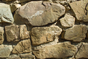 Fototapeta premium Frontal view of a wall of brown cement-bonded stones on a sunny day with deep shadows