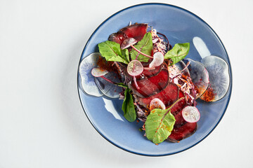 Traditional Italian appetizer bresaola beef jerky on lettuce leaves in a dark plate on a light background, top view, copy space