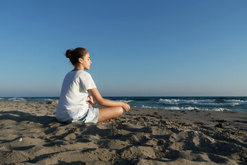 Fototapeta na wymiar Beautiful young woman meditates by the sea. Calmness and unity with nature.