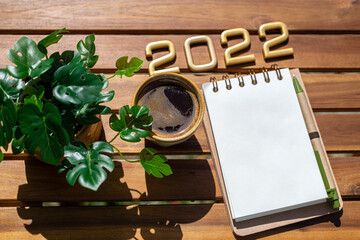 New year goals 2022 on desk. 2022 goals list with notebook, coffee cup, plant palm on wooden table. Resolutions, plan, goals, checklist, idea concept. New Year 2022 template, copy space