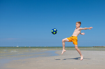 Happy teen boy playing with ball on beach at summer sunny day with blue sky