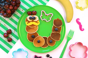 Caterpillar shaped pancakes with berries on green plate, top view. Healthy food for children. Funny food for kids.