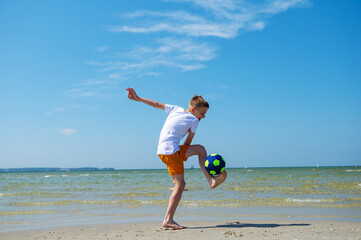 Happy teen boy playing with ball on beach at summer sunny day with blue sky