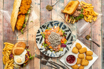 Freshly made food set. Seafood salad with salmon, eel and surimi, tuna and asparagus sandwich, chicken nuggets, breaded chicken sandwich and forks and spoons