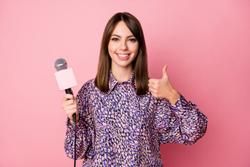Photo portrait of journalist with microphone showing thumb up isolated on pastel pink colored...