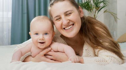 Portrait of smiling happy mother embracing her little baby boy in bed at morning. Concept of parenting ,baby care and family happiness