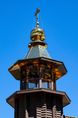Fototapeta na wymiar Picturesque bell tower of a wooden Orthodox church with a gilded roof and a cross