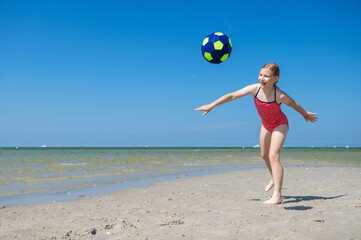 Cute teen girl playing and having fun with ball on beach at sunny summer day