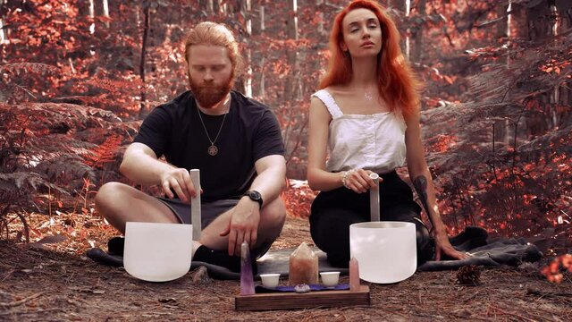 Red-haired couple playing on white quartz crystal singing bowls in the forest. Healing medicine and meditation Spiritual music Buddha