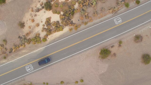 TOP DOWN: Flying above Route 66 as the lone tourist car drives along the famous straight highway. Drone point of view of the scenic highway crossing the rugged landscape of rural California, USA.