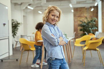 Know it all. Portrait of cheerful boy smiling at camera, standing with arms crossed while posing for camera during crafting classes