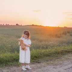 Naklejka na ściany i meble little girl with teddy bear on road at sunset