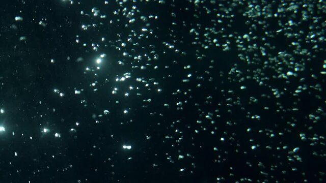 A beautiful texture of oxygen bubbles glowing in the dark water. Cosmic landscape with glittering particles and slow motion movement. Blue green spheres glistening in light on black space backdrop.