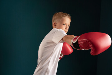 a young man in white clothes with blond hair boxing in red boxing gloves on a dark background. the...