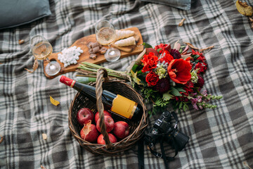 Still life. Basket with flowers, fruits and a bottle of wine on a blanket. Dinner with alcohol in nature