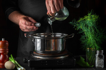 The cook adds oil to saucepan while making dumplings. Working environment on vintage kitchen table in restaurant.
