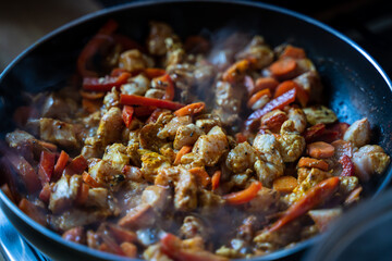 Vegetable stew, cooking chicken with vegetables. Process of cooking. Frying pan with vegetables and chicken meat on an induction cooktop, Macro shot of hot spicy turmeric Indian cuisine with steam