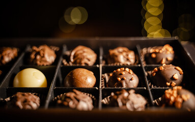Delicious chocolate candies or truffle balls in box on table against light bokeh. Assorted Chocolate pralines.An assortment of fine chocolates in white, dark, and milk chocolate with nuts.