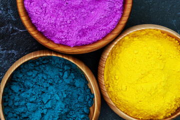 Top view of colorful bright traditional holi paint powder in wooden bowls isolated on dark concrete background. Copy space for text. Happy holiday. Concept of Indian color festival called Holi.