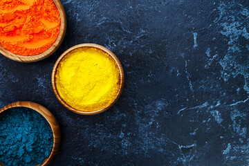 Top view of colorful bright traditional holi paint powder in wooden bowls isolated on dark concrete background. Copy space for text. Happy holiday. Concept of Indian color festival called Holi.