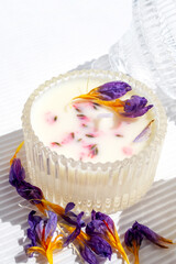 Organic wax candle in glass jar with dry flowers on white background. Homemade decor diy macro concept.