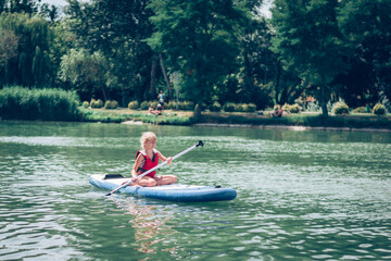 brave child on paddle board having fun and adrenaline on pond