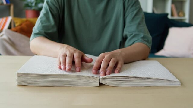 Blindman reading braille book using his fingers, sitting in living room, poorly seeing person learning to read, home education for people with disabilities, touching letters on sheet of paper.