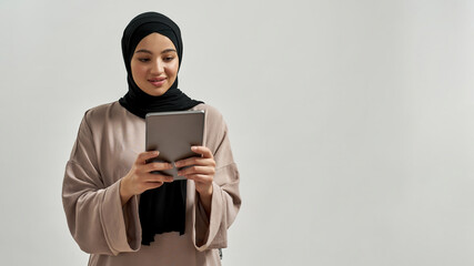 Cute young arabic woman in hijab looking into tablet