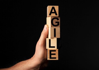 AGILE word on wooden blocks in male hand over black background with copy space for text.
