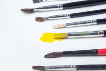 Fototapeta premium Paint brushes on a white background. One brush with yellow paint. Watercolor paint