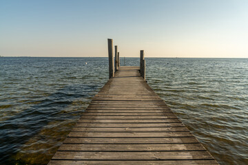 Fototapeta premium wooden dock leading out into a calm blue ocean in evening light