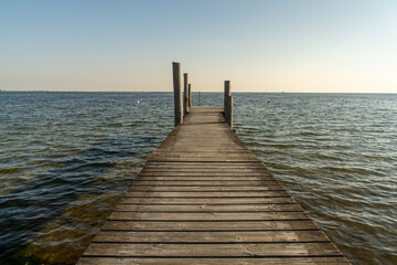 wooden dock leading out into a calm blue ocean in evening light